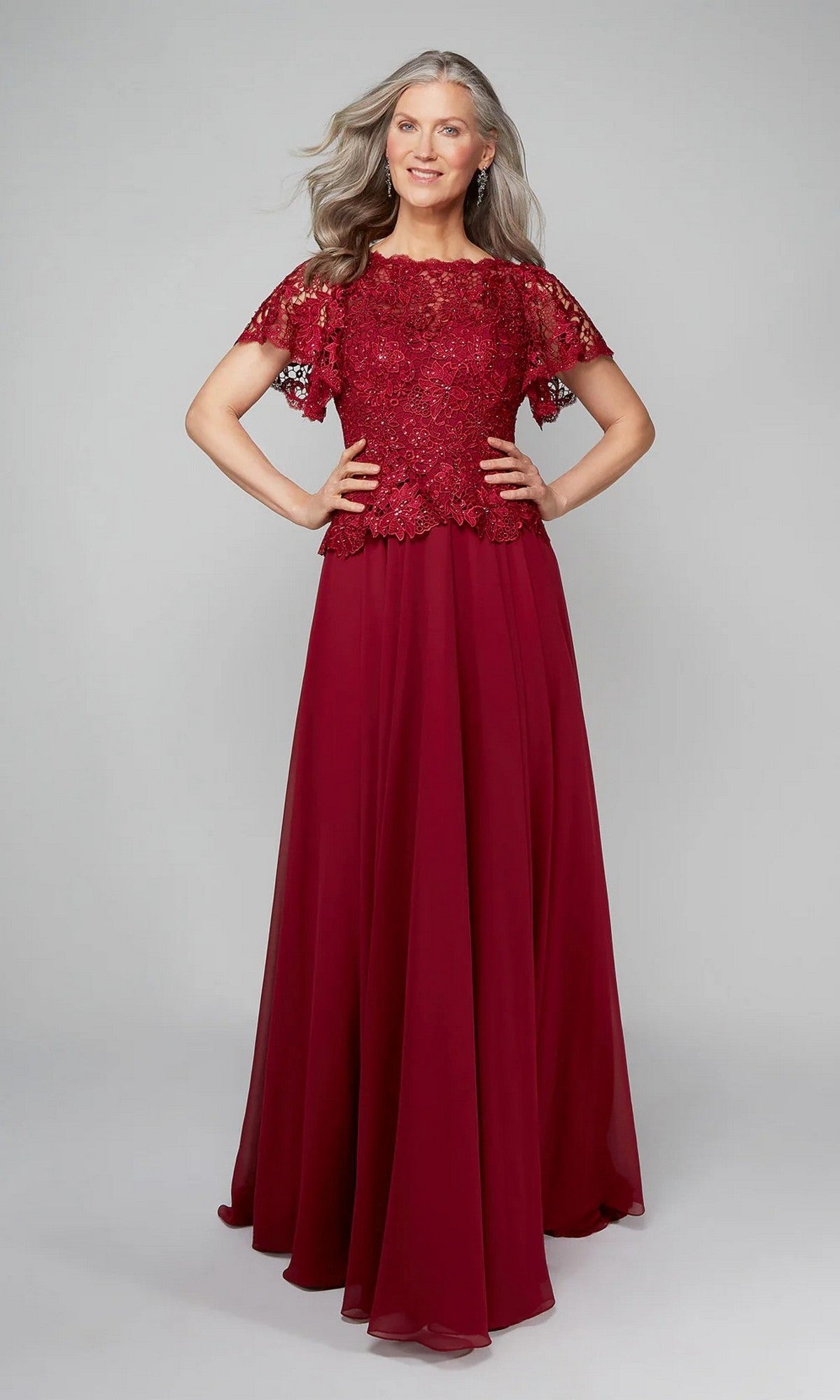 A woman with long gray hair models the Alyce 27469 long formal dress in wine, featuring a lace bodice and short sleeves, standing with hands on hips against a plain background.